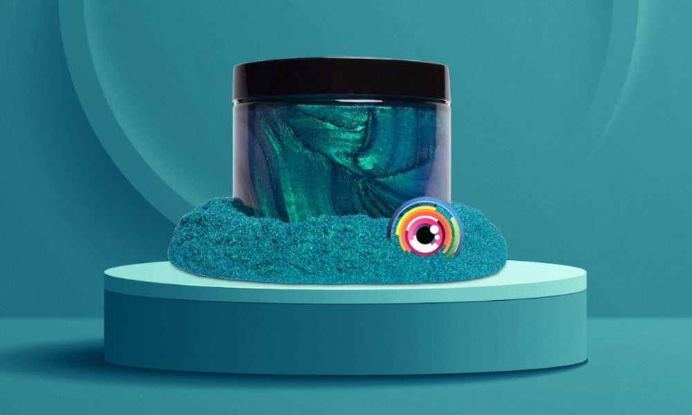 A jar of teal color-shift pigment sits on a round teal platform. Loose teal pigment is spread around its base.